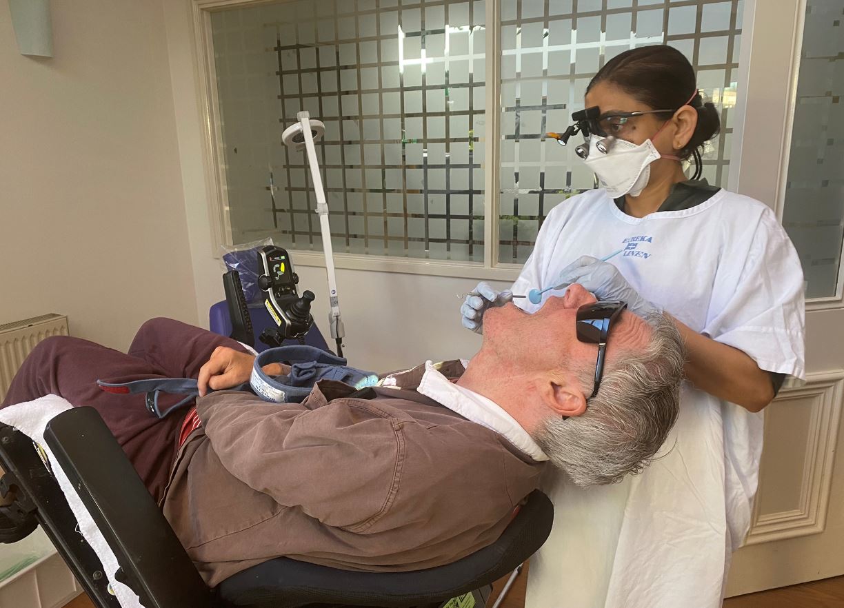 Aged Care Resident, Alan Berriman, receives a check-up in his wheelchair at his residential aged care home by dentist Dr Renuka Basavarajappa Maladihall.